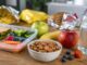 Tazón con almendras naturales junto a frutas y lonchera saludable sobre una mesa de cocina.