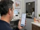 Persona realiza una prueba auditiva con audífonos inalámbricos y un teléfono, con equipo de audiología al fondo.