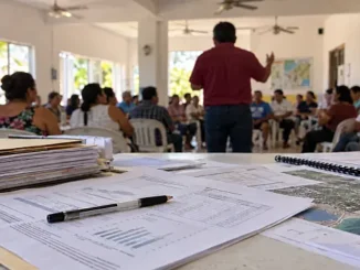 Documentos administrativos en primer plano durante una reunión comunitaria, imagen ilustrativa de la rendición de cuentas y las aspiraciones políticas.