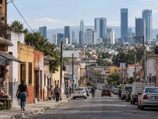 Calle de una zona popular de México, con viviendas deterioradas y pequeños comercios en primer plano y modernos rascacielos al fondo, reflejo de la desigualdad económica.